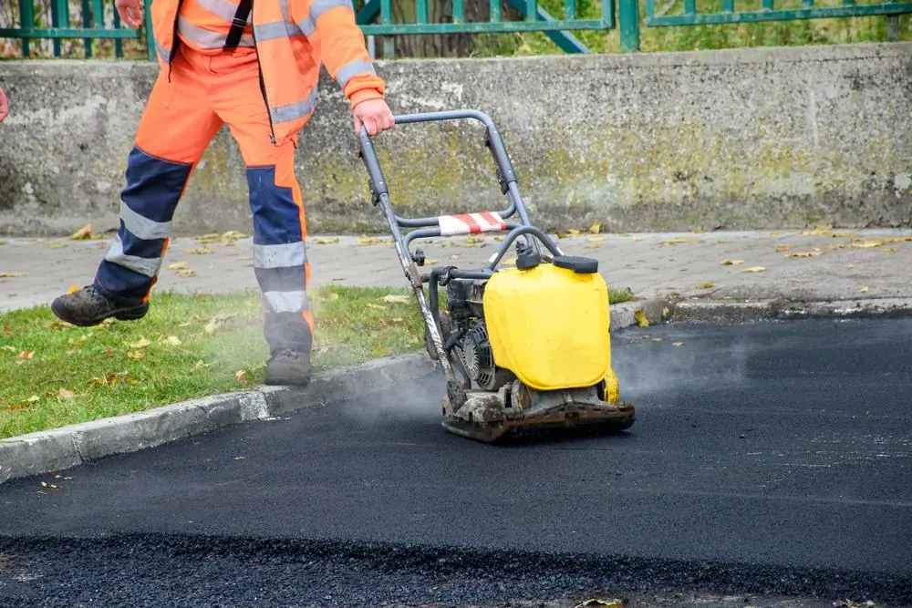 Worker compacting fresh asphalt with a plate compactor