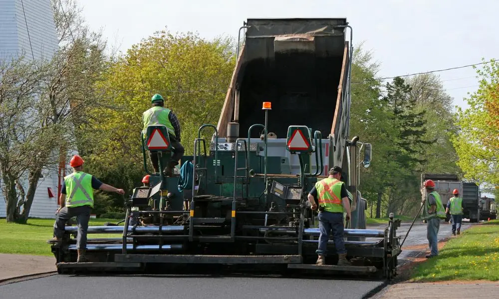Paving crew placing asphalt with a paver and dump truck