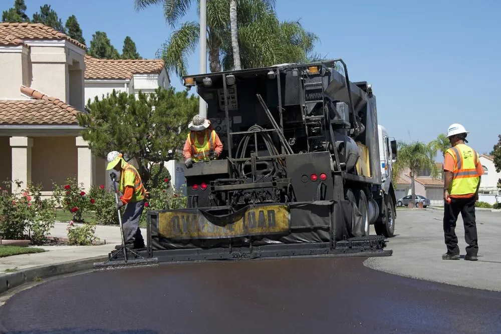 Asphalt paving equipment and crew working beside residential properties