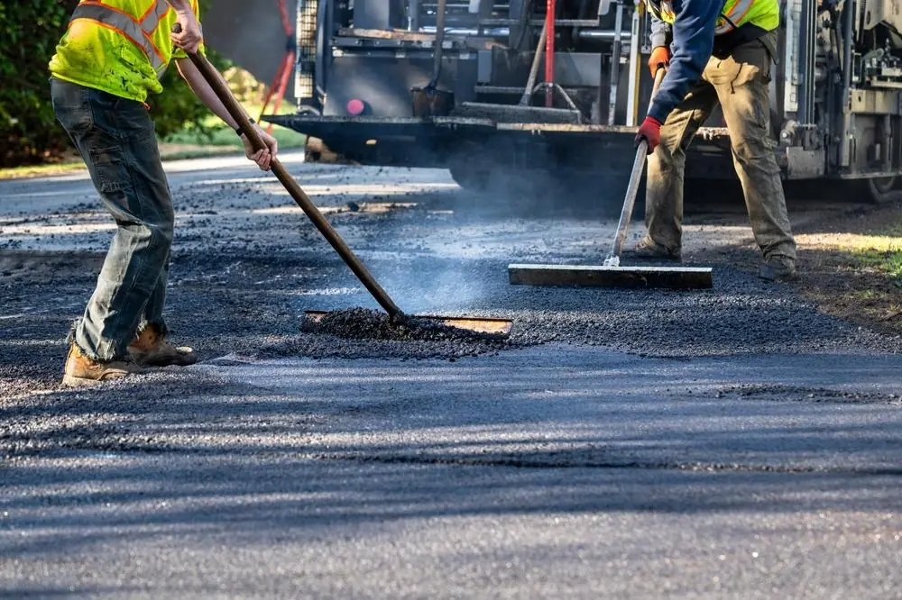 Workers raking and finishing freshly placed asphalt