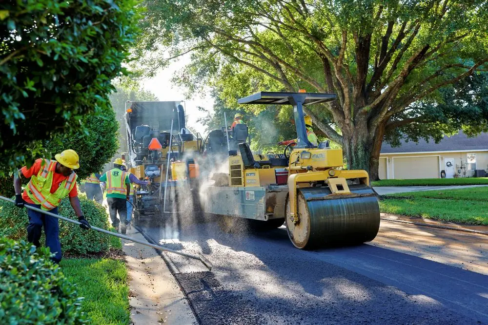 Paving crew and rollers working along a tree-lined road