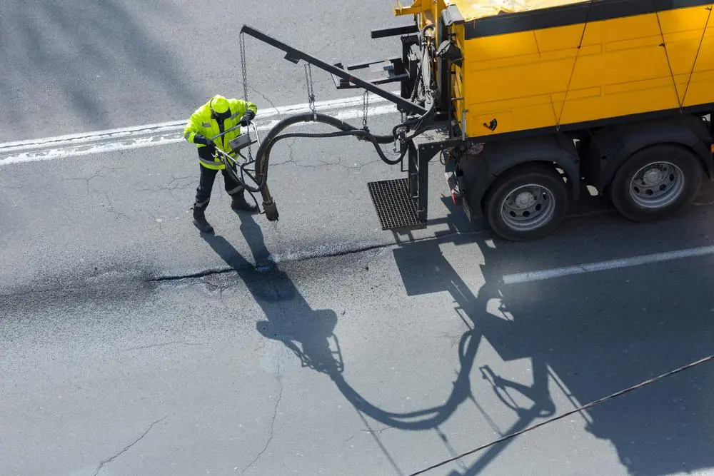 Workers applying a protective coating to asphalt beside a service truck