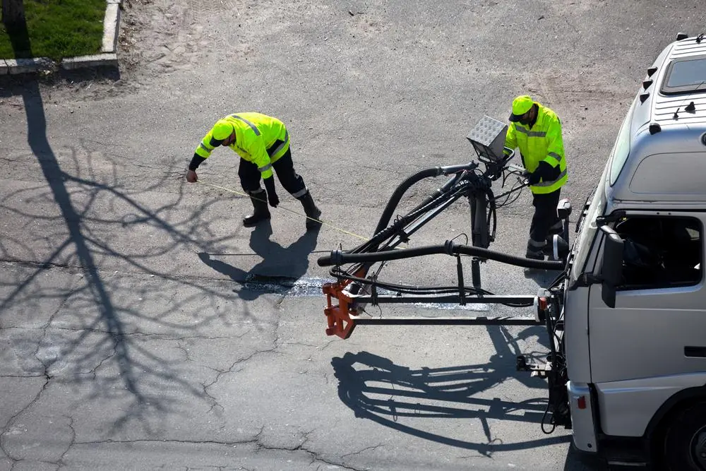 Workers treating an asphalt surface with a truck-mounted spray system